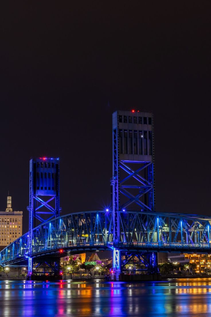 a bridge that is going over the water with lights on and buildings in the background