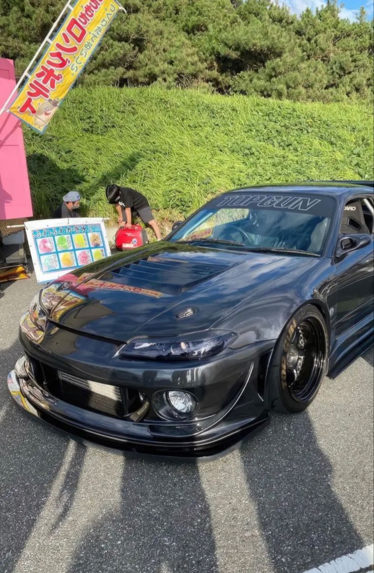 a black sports car parked in front of a sign with japanese writing on it's side