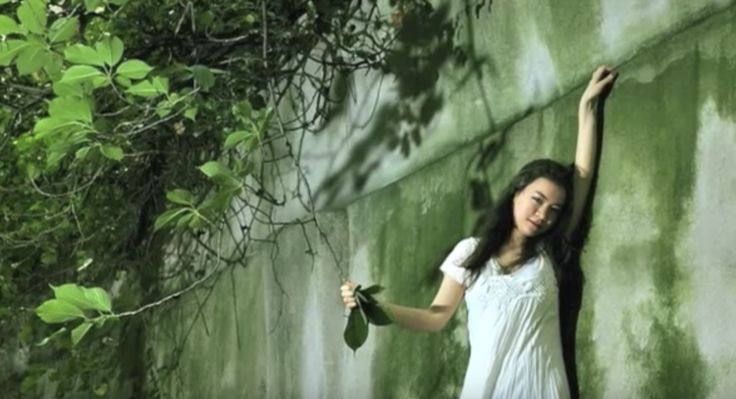 a woman leaning against a green wall with her arms in the air