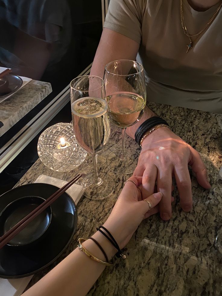 two people holding hands at a table with wine glasses and chopsticks on it