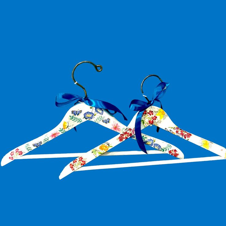 two white hangers with colorful flowers and blue ribbons on them against a blue background