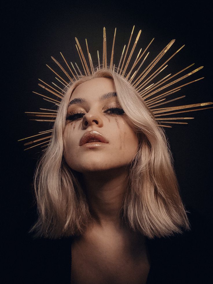 a woman with long blonde hair and gold spikes on her head, looking down at the camera