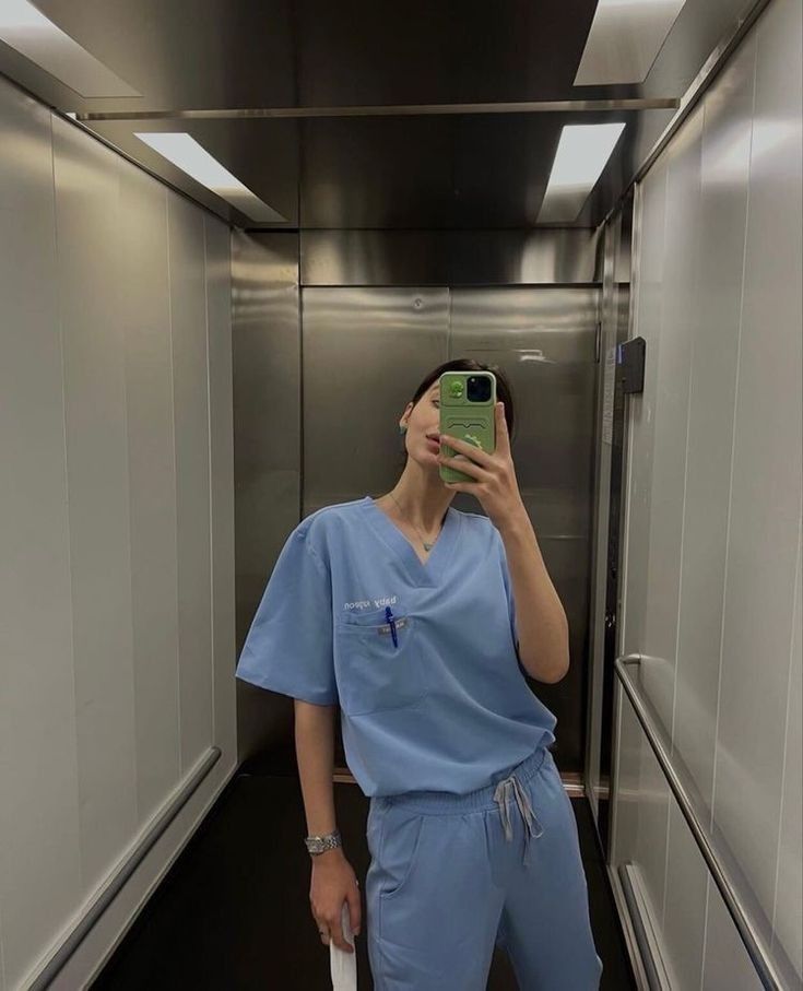 a woman in scrubs taking a selfie with her cell phone while standing in an elevator