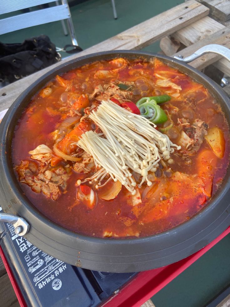 a bowl of soup with noodles, meat and vegetables in it on a picnic table