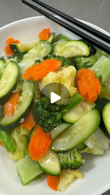 a white plate topped with cucumbers and carrots next to chopsticks