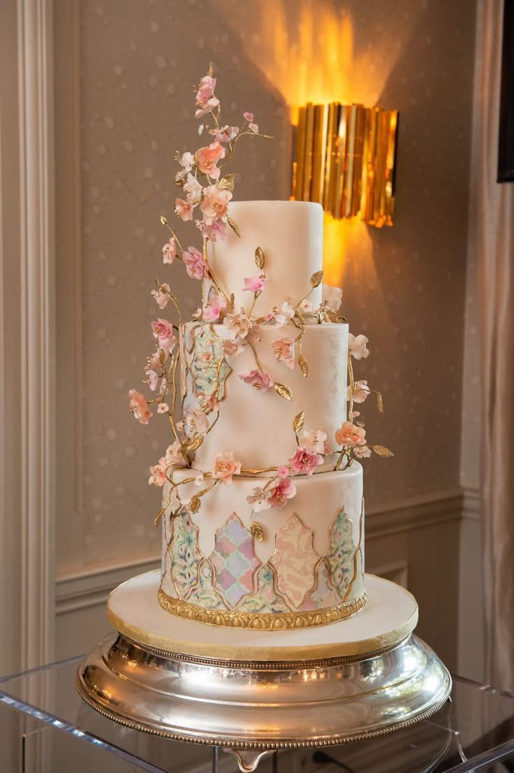 a three tiered wedding cake with pink flowers on the top and gold trimmings