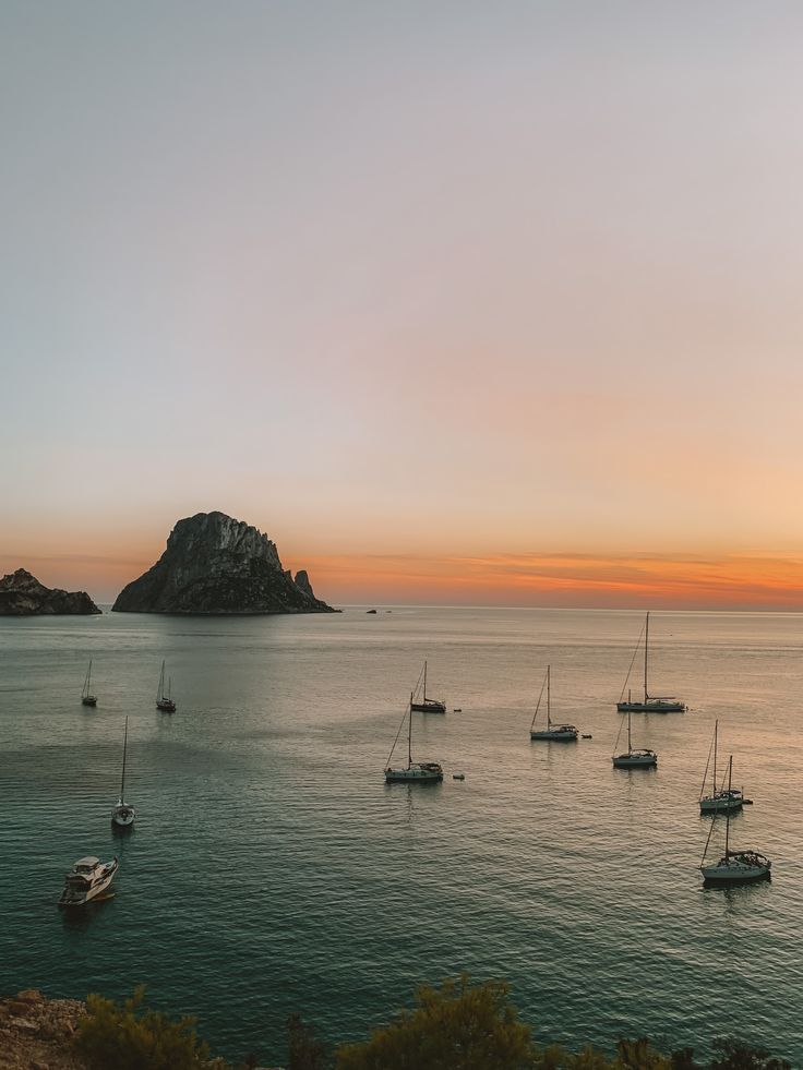 several sailboats floating in the ocean at sunset