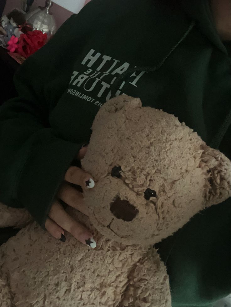 a person holding a brown teddy bear in their hands and wearing a green hoodie