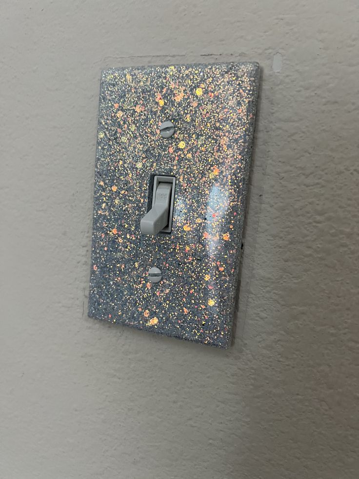 the light switch is covered in glitter and has a black cover with yellow, orange, and pink flecks on it