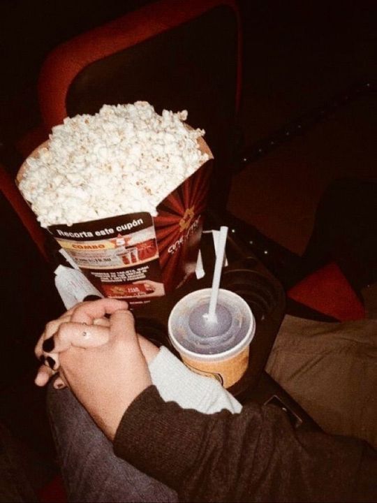 a person sitting in a chair holding a cup and popcorn