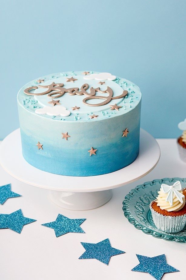 a blue and white cake sitting on top of a table next to cupcakes