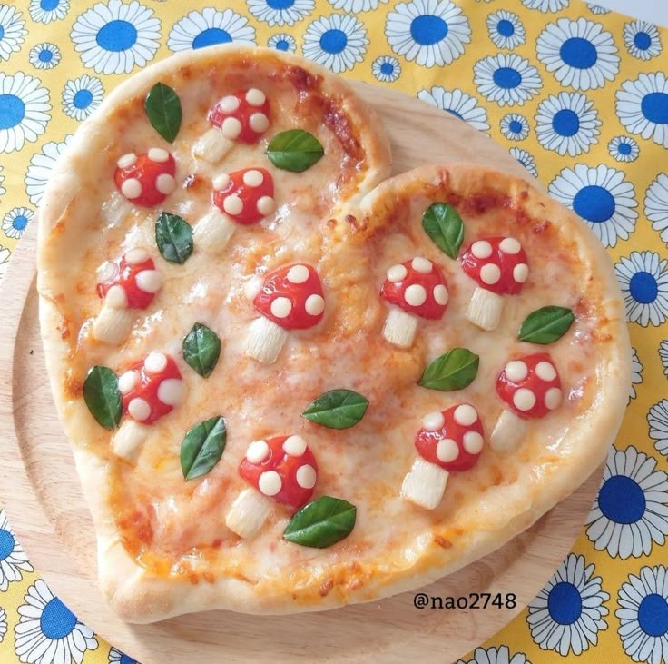 two heart shaped pizzas with mushrooms and basil on them sitting on a wooden plate