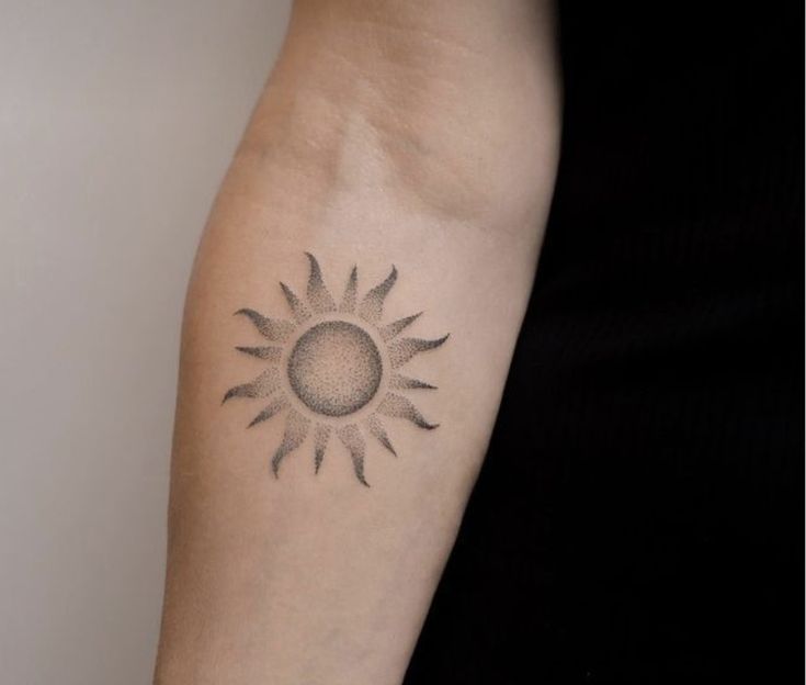 a woman's arm with a small sun tattoo on the left side of her arm