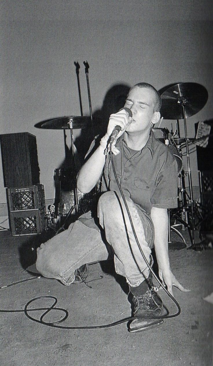 a young man sitting on the ground while holding a microphone to his ear and singing