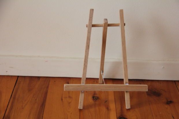 a small wooden easel sitting on top of a hard wood floor next to a wall