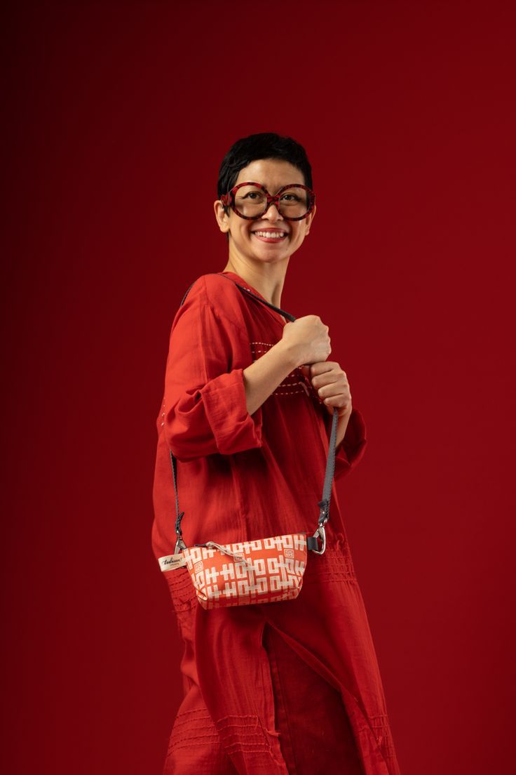 a woman with glasses and a red dress is holding a white purse in her hand