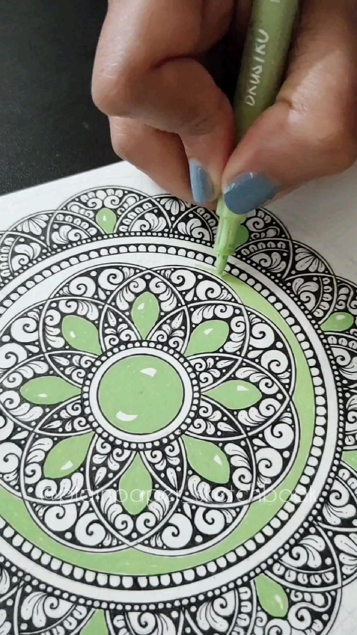 someone is using a marker to draw an intricate design on paper with green and white ink