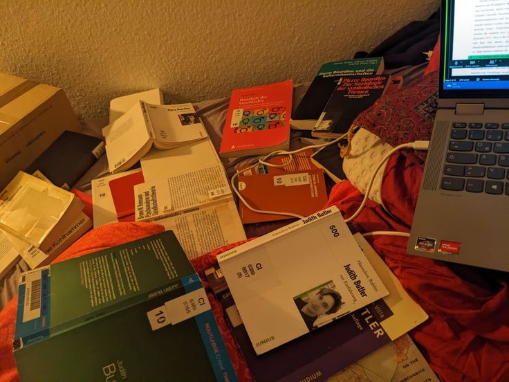 an open laptop computer sitting on top of a bed covered in books and other items