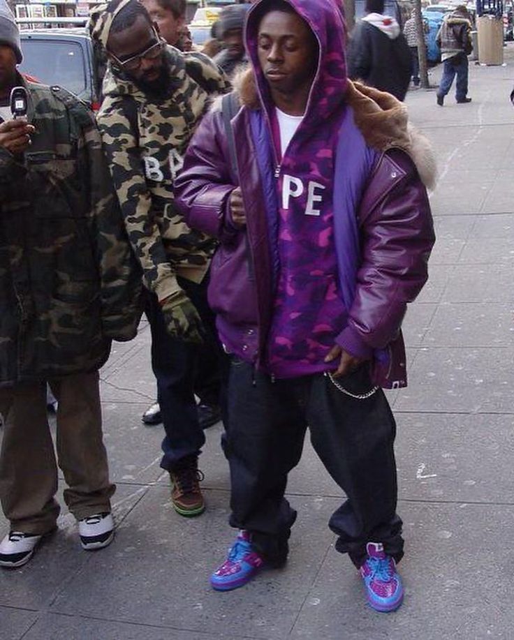 a man in a purple jacket is standing on the sidewalk with other people looking at his cell phone