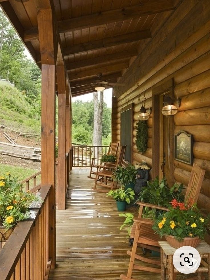 a porch with rocking chairs and potted plants on the front steps, next to a log cabin