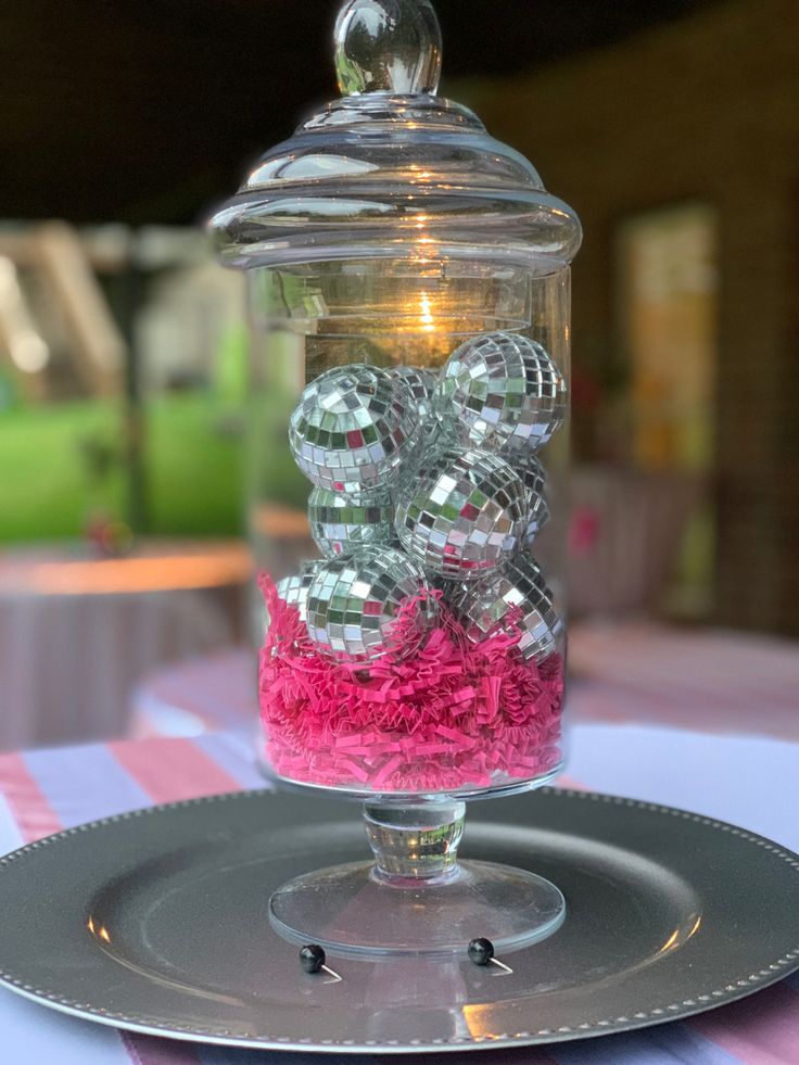 a glass jar filled with candy sitting on top of a silver plate next to a candle