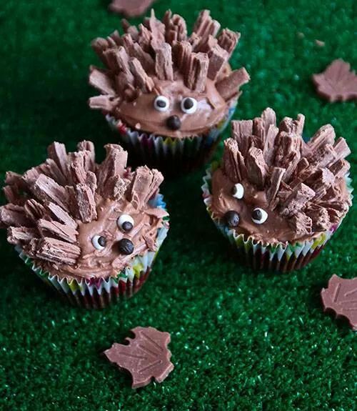 three cupcakes decorated like hedgehogs with chocolate frosting on green grass