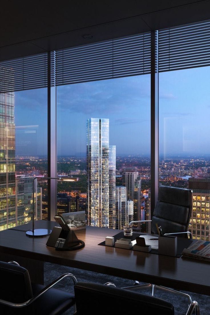 an office desk in front of large windows overlooking the city at night with skyscrapers lit up