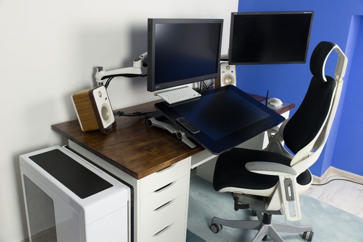 a computer desk with two monitors and a laptop on it, in front of a blue wall