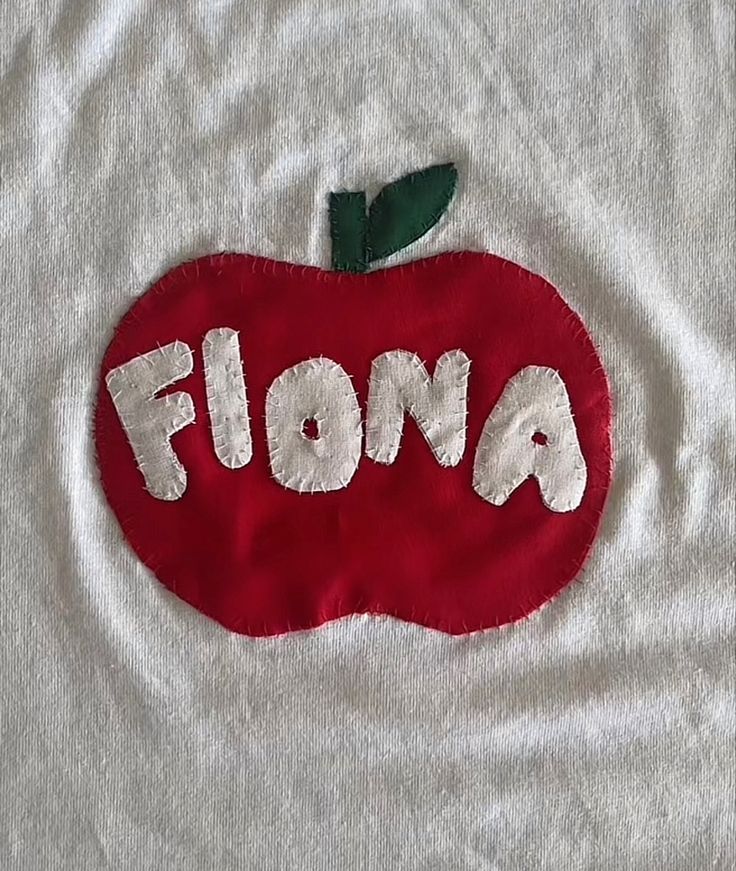 a red apple with the word flora painted on it's side, sitting on top of a white t - shirt