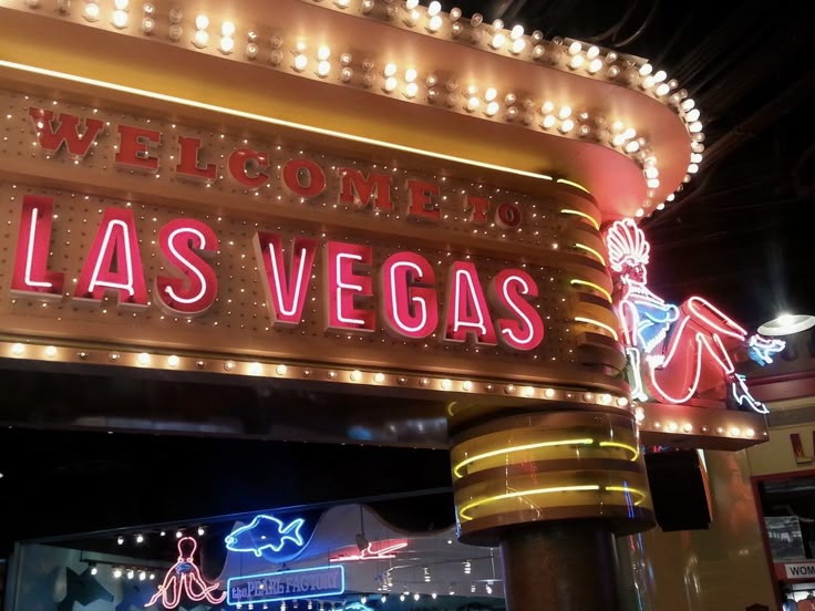 a sign that says welcome to las vegas in front of a building with lights on it