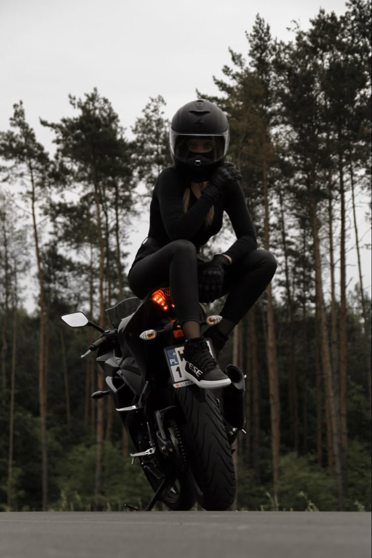 a person riding on the back of a motorcycle in front of some tall pine trees