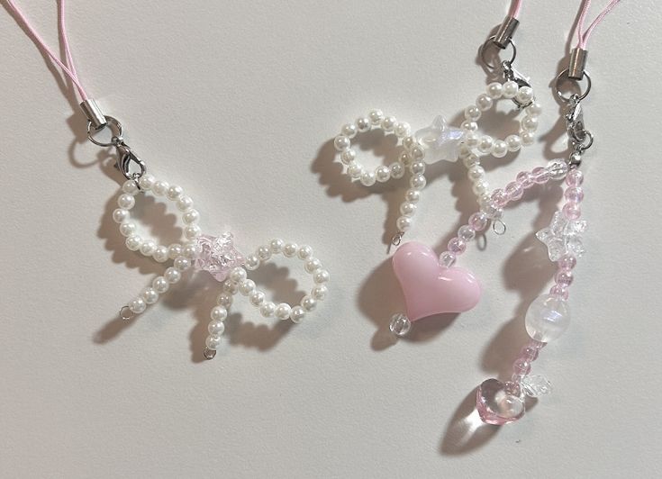 three necklaces with beads and charms attached to them on a white surface, one is shaped like the word love