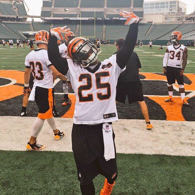 a football player holding his arms up in the air with other players on the field behind him