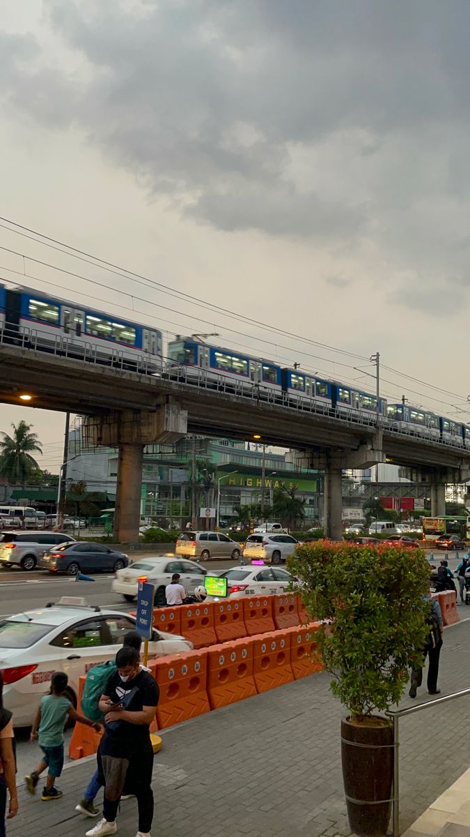 people are walking on the sidewalk in front of an overpass with cars and trains