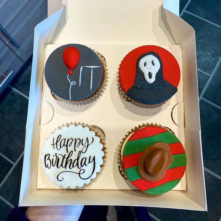 three decorated birthday cupcakes in a box