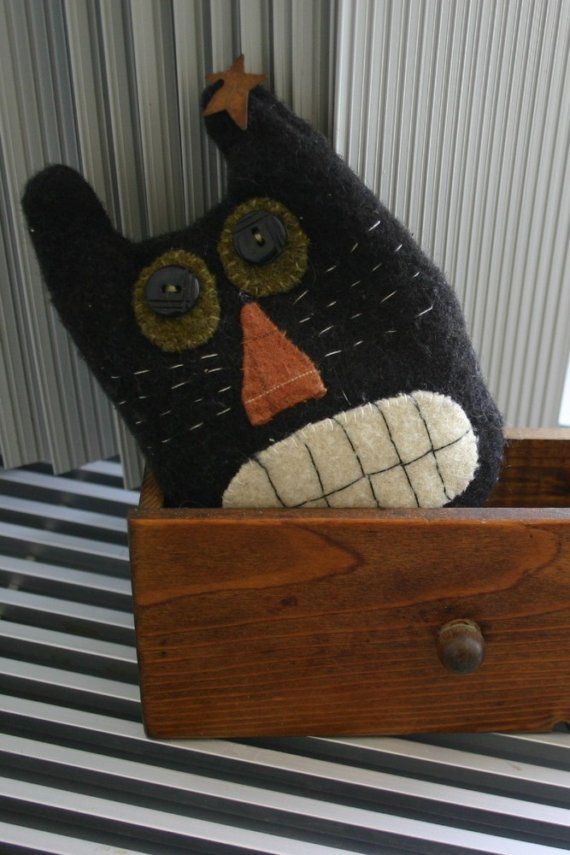 a black cat stuffed animal sitting in a wooden box on top of a striped table cloth