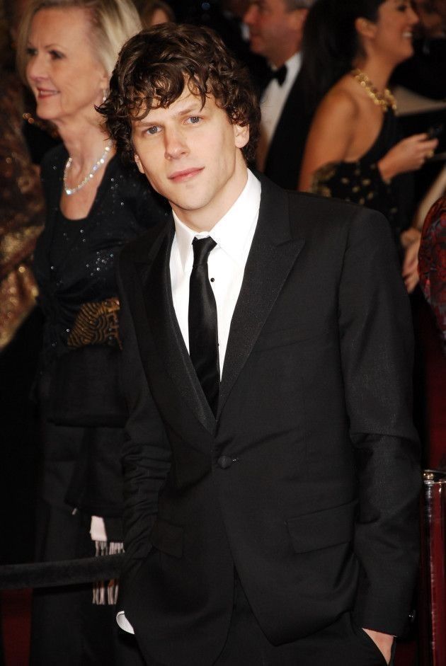 a young man in a black suit and tie at an event with other people behind him