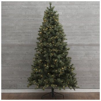 a small christmas tree with lights on it in front of a gray wall and wooden floor