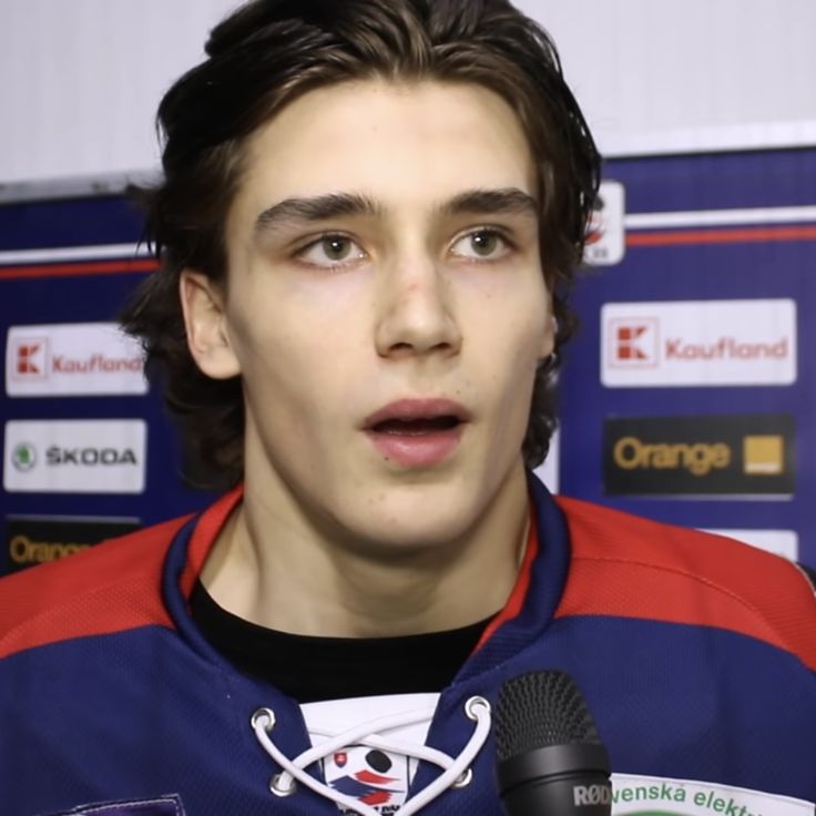 the young man is talking to the camera in front of a microphone and wearing a red and blue jacket