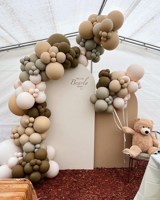 a teddy bear sitting in front of a balloon arch