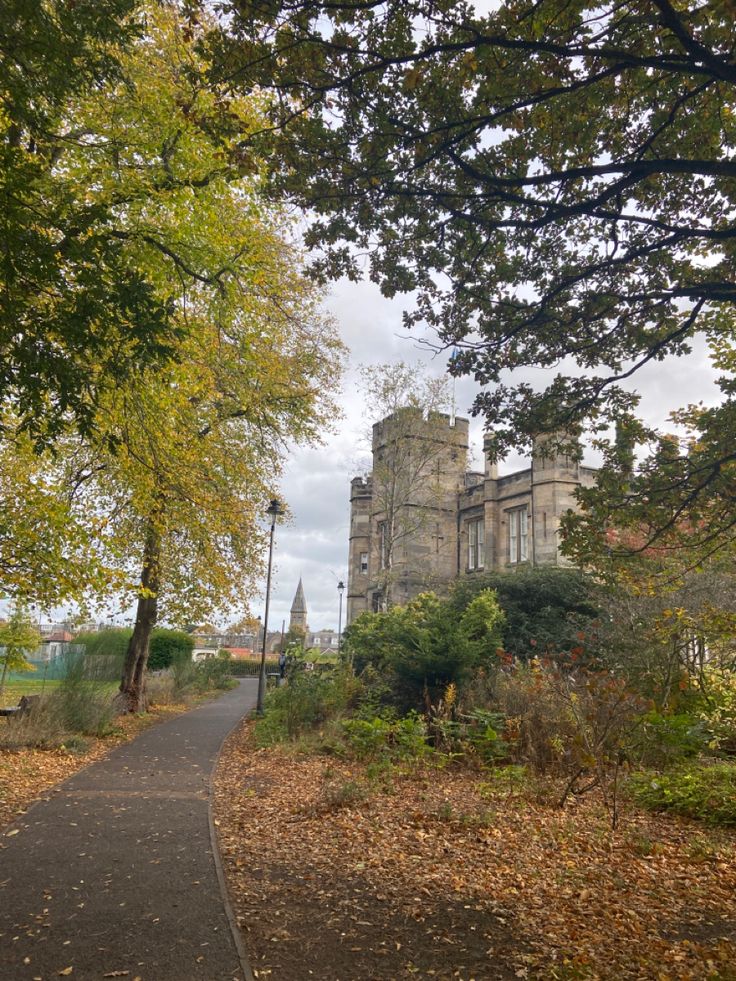 an old castle sits in the distance with trees around it and leaves on the ground