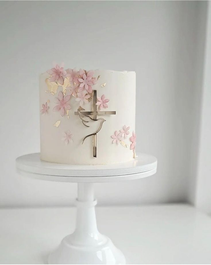 a white cake decorated with pink flowers and a cross on the top is sitting on a pedestal