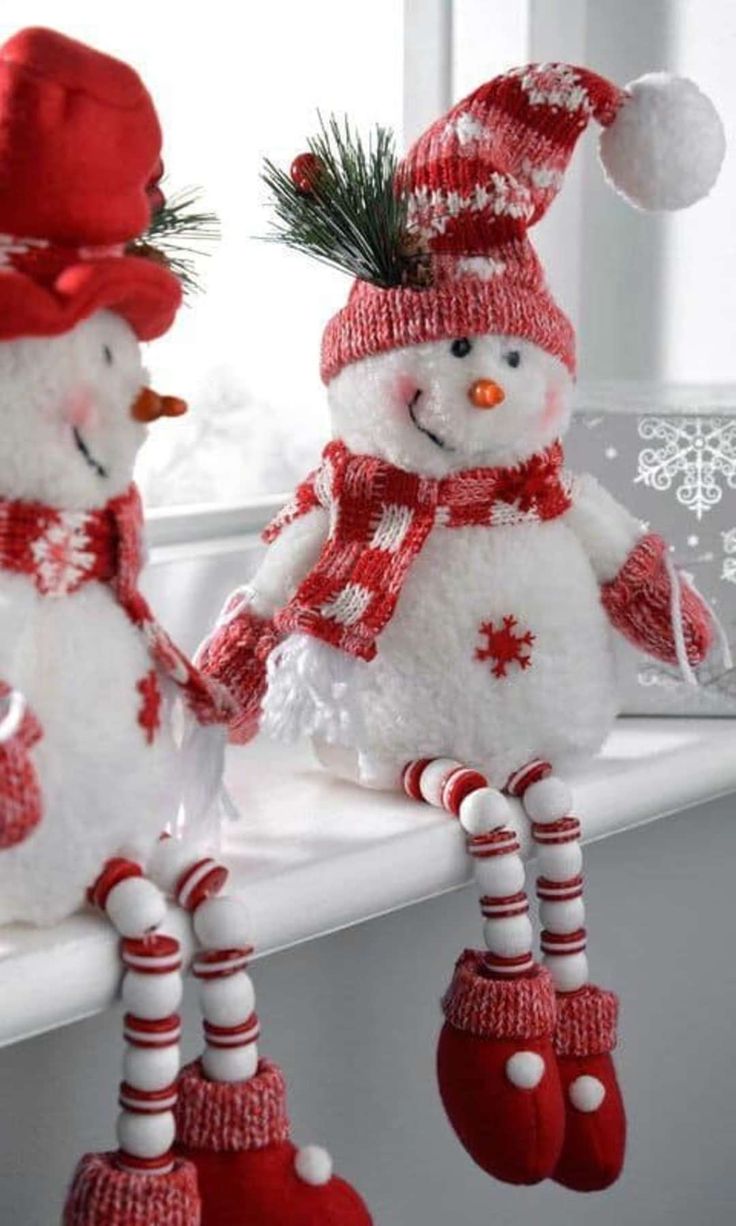 two snowmen sitting on top of a window sill wearing red hats and scarves