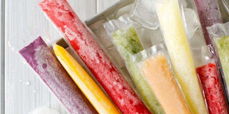 four different types of fruit sticks in plastic wrappers on a white wooden table with mint leaves