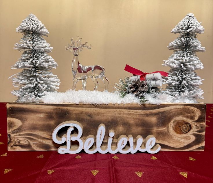 a wooden sign that says believe and two deers in the snow with pine trees behind it