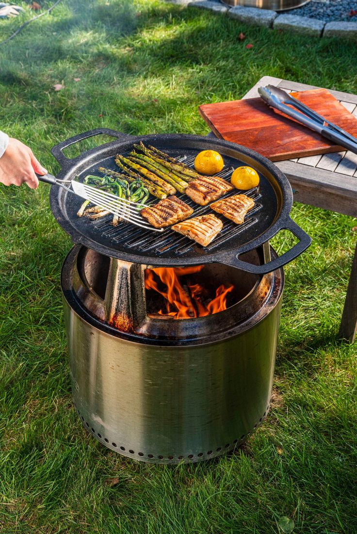 a person is grilling food on an open fire pit in the grass near a picnic table