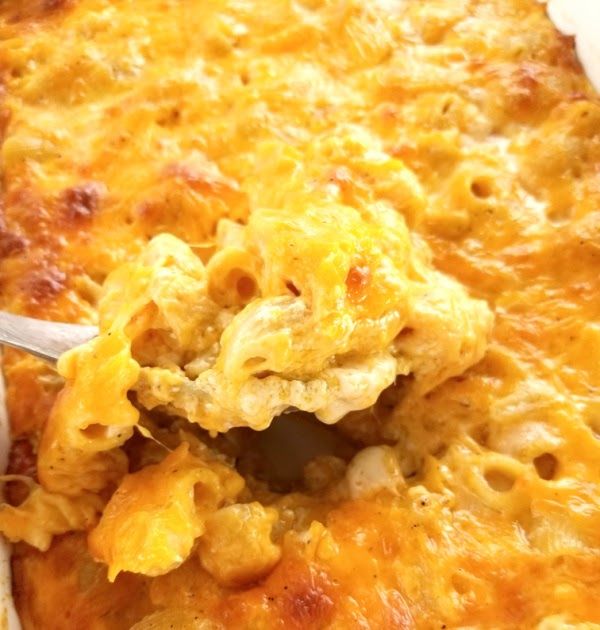 a spoon full of macaroni and cheese being lifted from a casserole dish