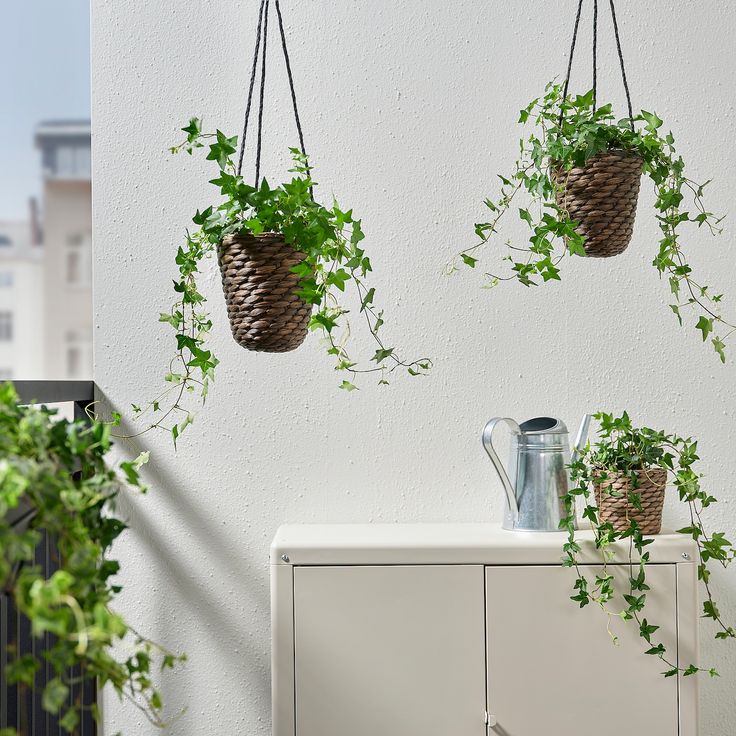 three hanging planters with plants in them on the side of a white wall next to a cabinet