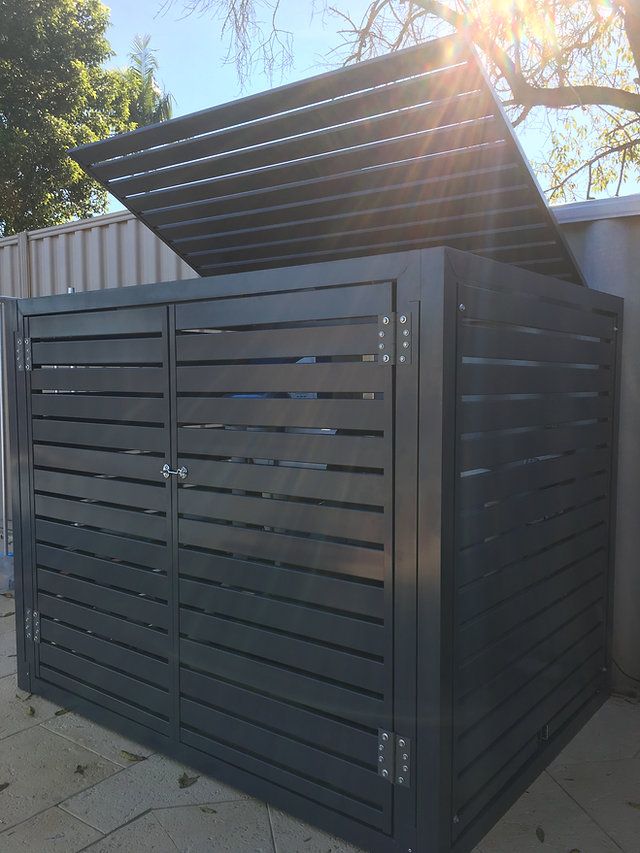 a large metal box sitting on top of a sidewalk next to a tree and fence