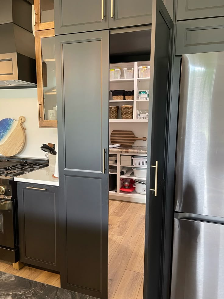 a kitchen with gray cabinets and stainless steel refrigerator freezer combo in the center, next to an open pantry door